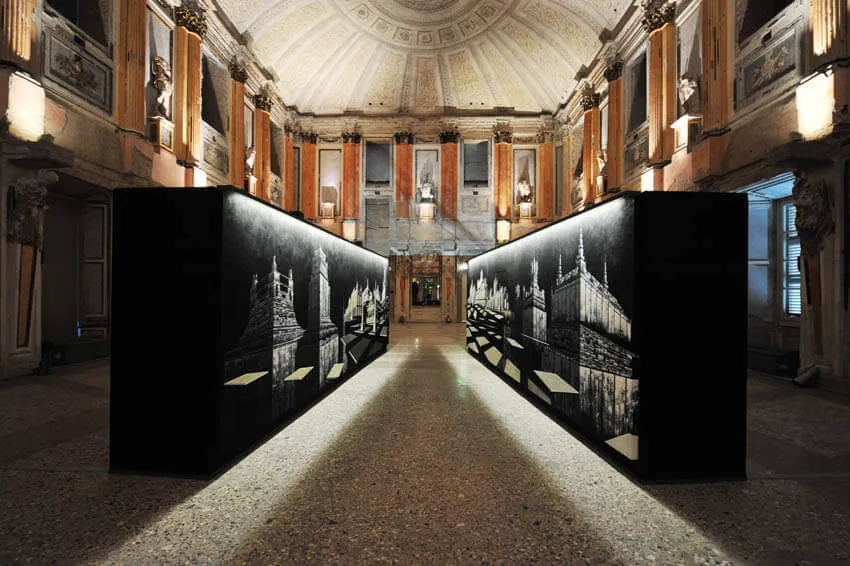 Allestimento in una sala storica: volumi neri retroilluminati inseriti sotto una volta affrescata